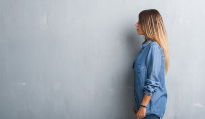 Young adult woman over grunge grey wall wearing denim outfit looking to side, relax profile pose with natural face with confident smile.