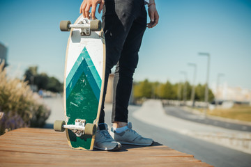 Close up of young man holding longboard or skateboard in the park.