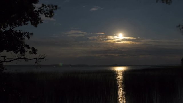 Moon in clouds on the lake, dramatic sky, time-lapse 4K.
