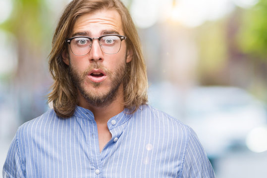 Young handsome man with long hair wearing glasses over isolated background afraid and shocked with surprise expression, fear and excited face.