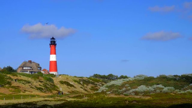 Leuchtturm H&ouml;rnum Sylt mit D&uuml;nen Landschaft  Reetdach H&auml;usern und  blauen Himmel
