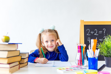 Happy cute industrious child is sitting at a desk indoors