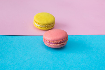 Obraz na płótnie Canvas Close up of pink macaron on blue and pink background. Yellow macaron on background. Selective focus