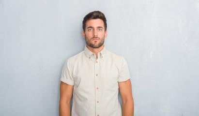 Handsome young man over grey grunge wall wearing summer shirt with serious expression on face....