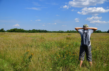 teenager with backpack is standing on meadow