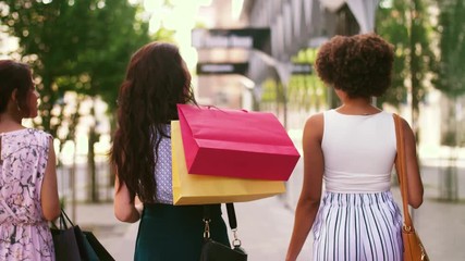 sale, consumerism and people concept - young women with shopping bags walking along city street - Powered by Adobe