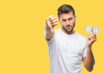 Young handsome man holding dollars over isolated background with angry face, negative sign showing...