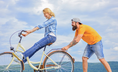 Obraz premium Girl cycling while man support her. Cycling service. Service and assistance. Mechanic helps maintain bicycle. Supportive service. Woman rides bicycle sky background. Man helps keep balance ride bike