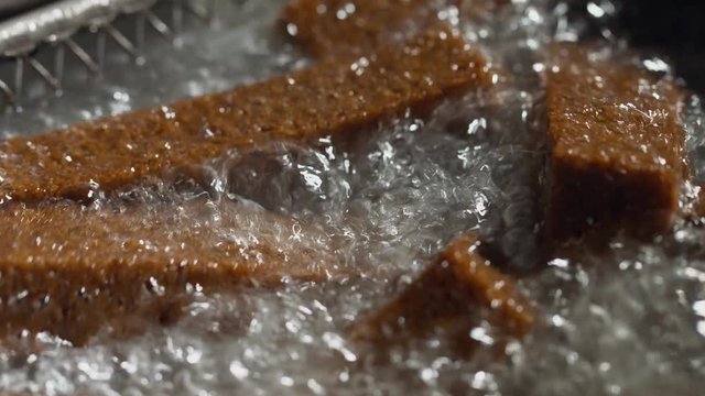 Preparation process of beer snacks in deep fryer. Close-up of deep-fried bread rusks. Macro shot. Breadcrumbs floating in boiling fresh oil in kitchen of bar or pub