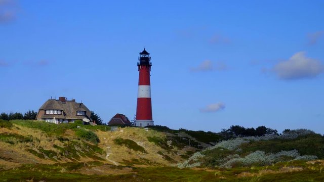 Leuchtturm H&ouml;rnum Sylt im Wechsellicht mit D&uuml;nen Landschaft  und blauen Himmel
