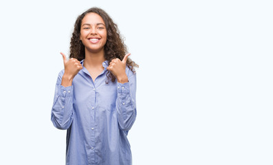 Young hispanic business woman success sign doing positive gesture with hand, thumbs up smiling and happy. Looking at the camera with cheerful expression, winner gesture.