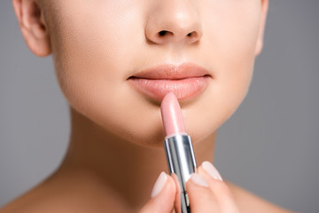 partial view of woman applying nude lipstick isolated on grey
