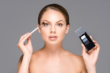 portrait of attractive woman with eyeshadows and makeup brush isolated on grey