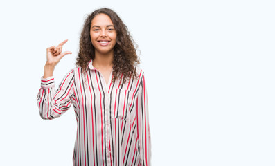 Beautiful young hispanic woman smiling and confident gesturing with hand doing size sign with fingers while looking and the camera. Measure concept.