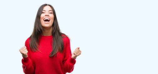 Young beautiful hispanic wearing red sweater celebrating surprised and amazed for success with arms...