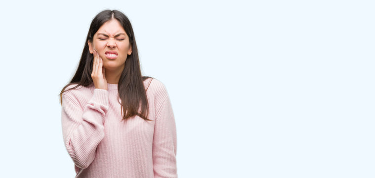 Young beautiful hispanic woman wearing a sweater touching mouth with hand with painful expression because of toothache or dental illness on teeth. Dentist concept.