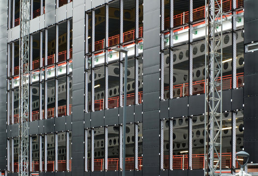 An urban construction site with cladding being fastened to the metal framework of a large commercial development with orange safety fences and large metal girders visible supporting the structure