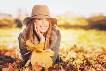 Obraz premium Gorgeous young woman in autumn in park with big yellow leaves, smiling and enjoying nature. Natural lighting, retouched, back light, closeup, copy space.