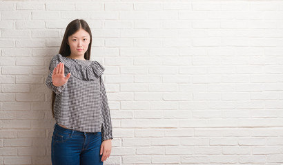 Young Chinese woman over brick wall with open hand doing stop sign with serious and confident expression, defense gesture