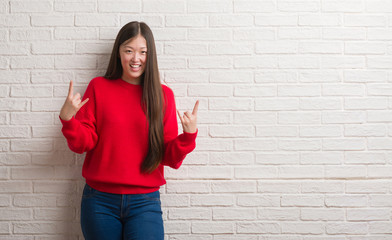 Obraz na płótnie Canvas Young Chinese woman over brick wall shouting with crazy expression doing rock symbol with hands up. Music star. Heavy concept.