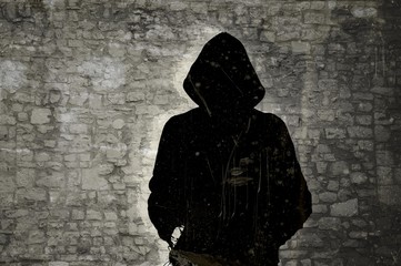 Male black and white figure with hood on stone wall background. Hacker concept.