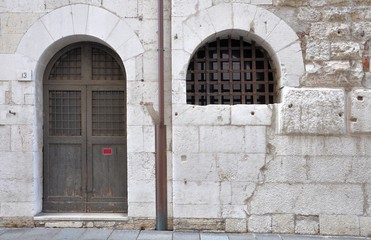 Gothic window and arched door with iron grating in ancient stone wall.