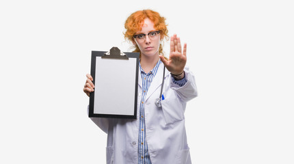 Young redhead doctor woman holding clipboard with open hand doing stop sign with serious and confident expression, defense gesture