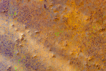 Rusty iron wall with spots of green, violet and yellow paint