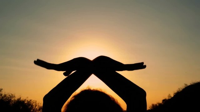 Silhouette of a girl with wings at sunset. The girl folded her hands over her head and waves them like wings against the yellow light. Close up. 4K. 25 fps.