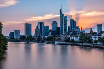 Fototapeta na wymiar Frankfurter Skyline während des Sonnenuntergangs über dem Main, Blick auf das Bankenviertel - Sonnenuntergang mit roten und blauen Pastellfarben