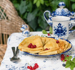 a dessert of crepes, in the garden, blue colour plate, cup of tea, vintage sugar pot, green wall of leafs as background
