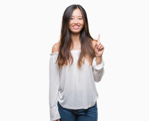Young asian woman over isolated background showing and pointing up with finger number one while smiling confident and happy.