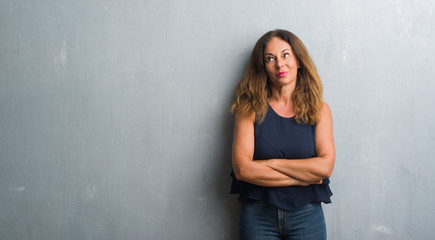 Middle age hispanic woman standing over grey grunge wall smiling looking side and staring away thinking.