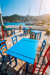 Fototapeta na wymiar Colorful table and chairs in a typical tavern by the sea. Greek fishing village at hot summer day
