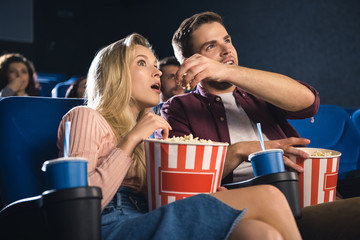 emotional couple with popcorn watching film together in cinema