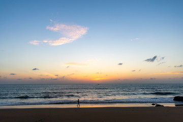 A landscape of a beach just after sunset with a person silhouette walking by, water in the background