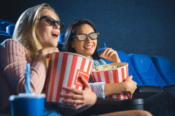 Naklejka premium emotional multiracial women in 3d glasses with popcorn watching film together in movie theater
