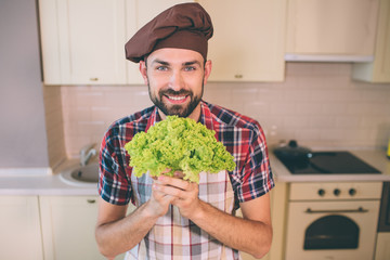 Nice and cheerful man stands and looks on camera. He is happy. Guy holds green letuce in hands. Man poses. He looks amazing.