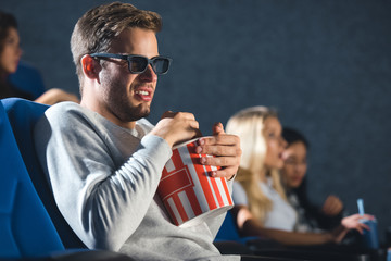 side view of disgusted man in 3d glasses with popcorn watching film in cinema