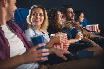 cheerful multiethnic friends with popcorn watching film together in movie theater