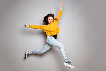 cheerful young woman jumping in the air against gray background