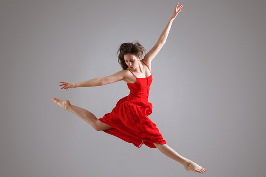 elegant dancer in red dress jumping against gray background