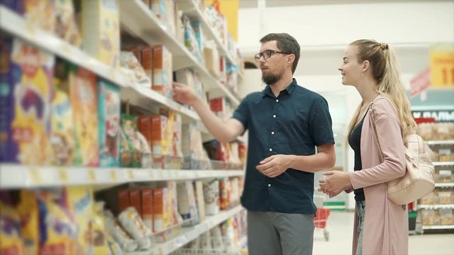 Man and woman are debating a cereal for cooking in a grocery department of supermarket. Husband is offering product and woman is deciding