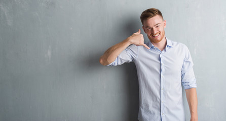 Young redhead business man over grey grunge wall smiling doing phone gesture with hand and fingers like talking on the telephone. Communicating concepts.