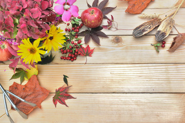 top view on autumnal flowers put on a wooden table with leaf, gardening tool and red apple 