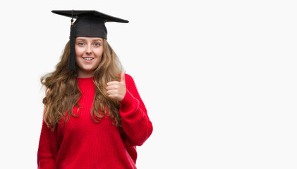 Young blonde woman wearing graduation cap happy with big smile doing ok sign, thumb up with fingers, excellent sign