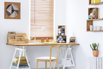 DIY yarn art on a white wall of a scandinavian crafts room interior and creative workspace with knitting tools. Real photo.