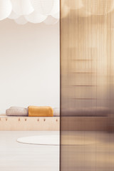 Orange blanket on wooden bed in minimal bedroom interior with rug and screen. Real photo