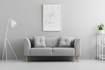 White lamp next to grey couch in minimal living room interior with poster and plant. Real photo