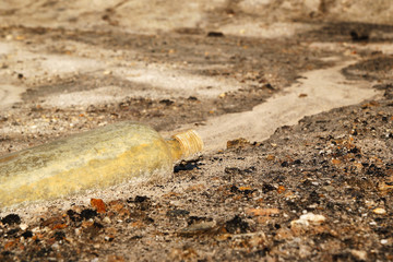 Obraz premium Old dirty glass bottle on a dry sandy soil.